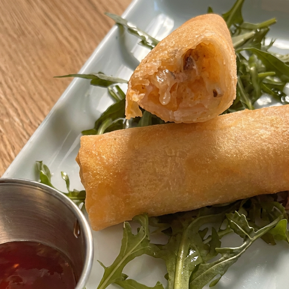 Golden fried spring rolls, one cut open, served with arugula and dipping sauce on a white plate.